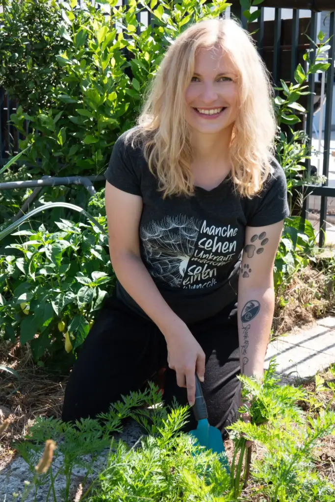 Frau sitzt kniend im Garten und ist mit einer Gartenschaufel am Gärtnern.