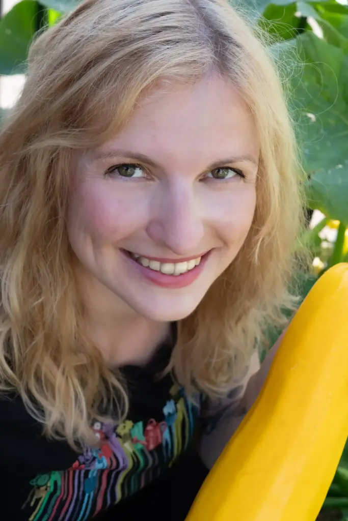 Nahaufnahme einer blonden Frau mit einer gelben Zucchini in der Hand. Es ist nur der Kopf sowie ein Ausschnitt des Gemüse zu sehen.