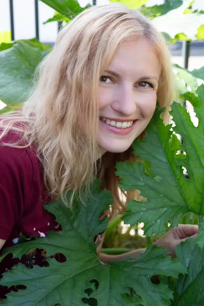 Julia im Garten bei einer großen Pflanze. Bild dient als Titelbild der über mich seite als Gartencoach.