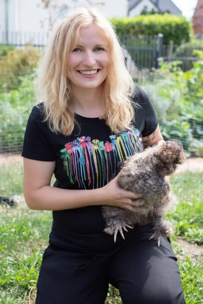 Lächelnde Frau in einem Garten hält ein flauschiges Huhn und zeigt ihre Begeisterung für Tier und Natur.