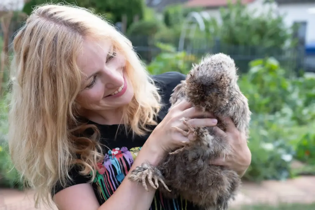 Frau mit Huhn auf dem Arm im Garten.